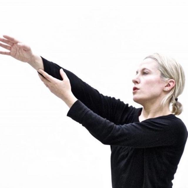 person in black shirt with blonde hair reaching arms out on a diagonal