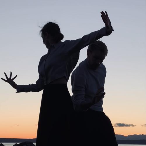 two dancers cast in silhouette against a pale grey and orange sky
