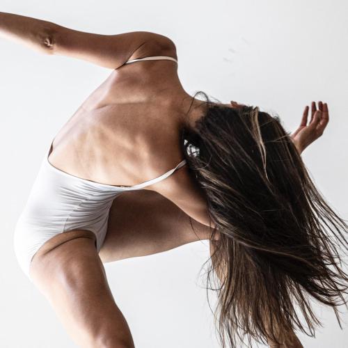 a photo of a dancer against a white background, their body is twisted and focus is facing back