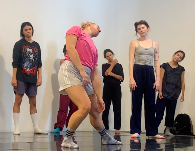 person bending to the left with pink shirt and gray shorts in dance studio with black floor