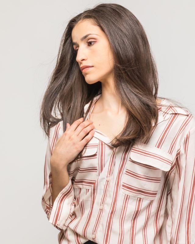 image of a woman in a multicolored striped button down with flowy brown hair focused downwards towards the corner