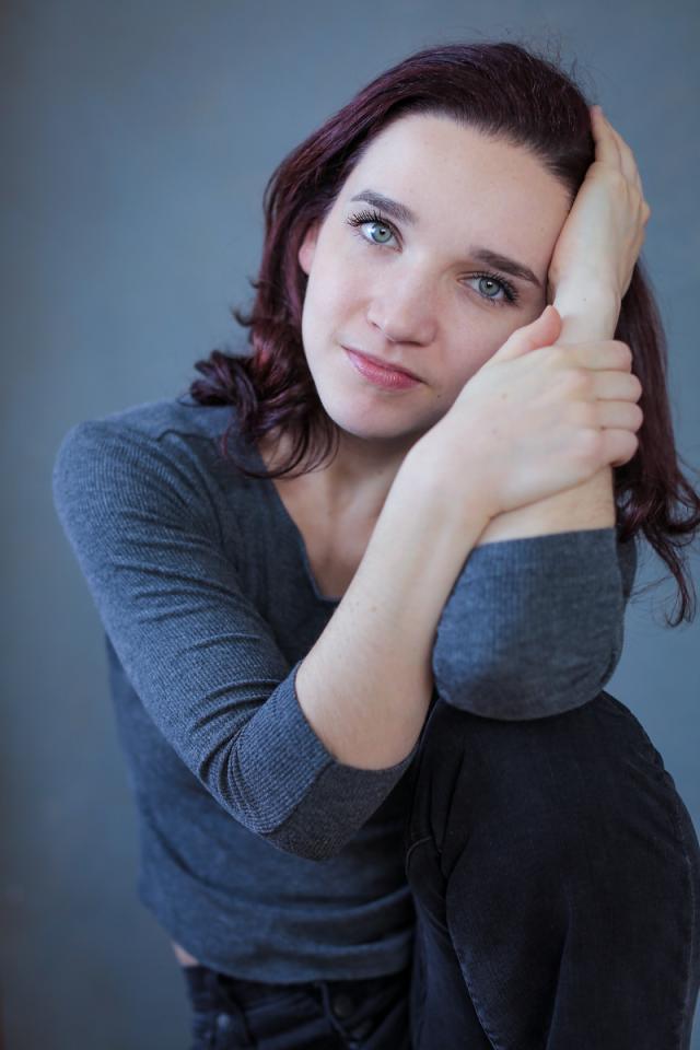 a photo of a person with shoulder length hair, and their hands caressing the side of their face wearing blue against a blue background