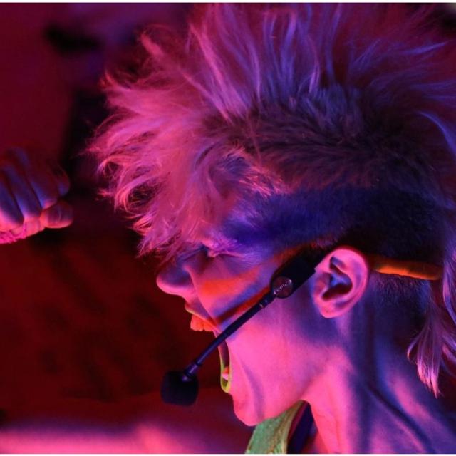 person looking to the side with blonde mohawk and fist raised looking into a bring pink light