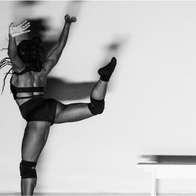 B&W photo of dancer with leg extended behind them and arms reaching above their head facing upstage