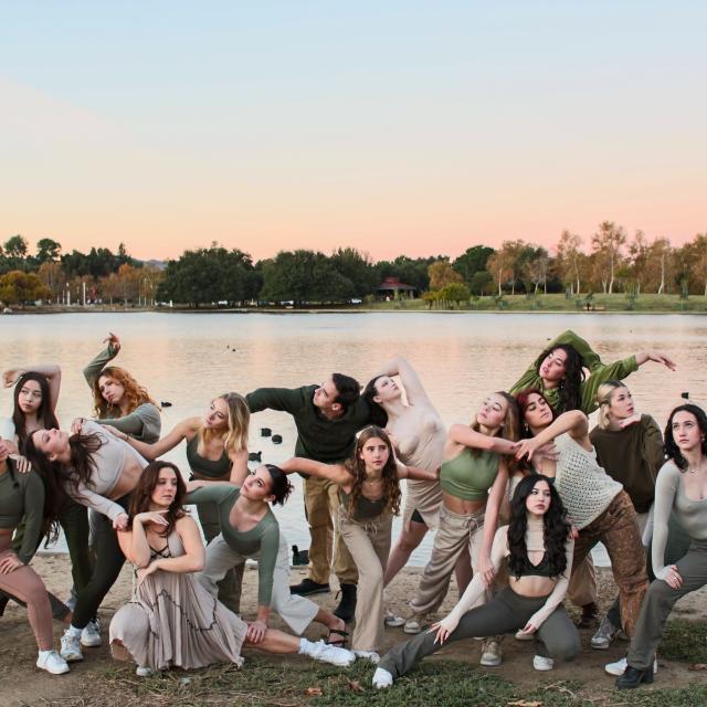 image of a large group of dancers melting into each other in various positions all wearing earth tone colors against a large pond in the background