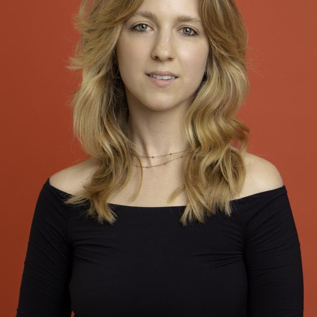 dancer with blonde hair wearing a black long sleeve shirt in front of a red backdrop
