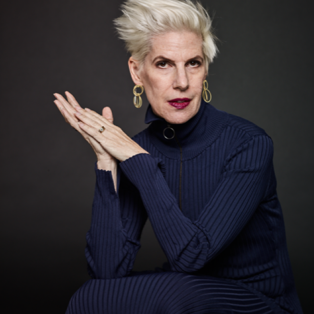 image of a person staring into the camera with white hair and a blue turtleneck
