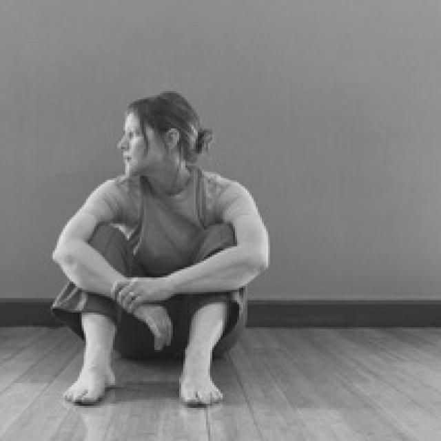 a black & white image of a woman sitting on the floor with their arms over their legs and looking profile 