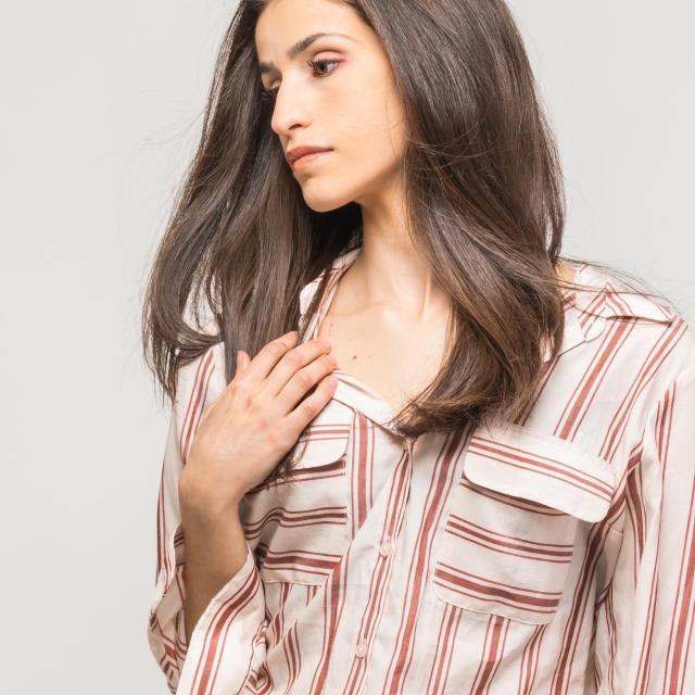 image of a woman in a multicolored striped button down with flowy brown hair focused downwards towards the corner