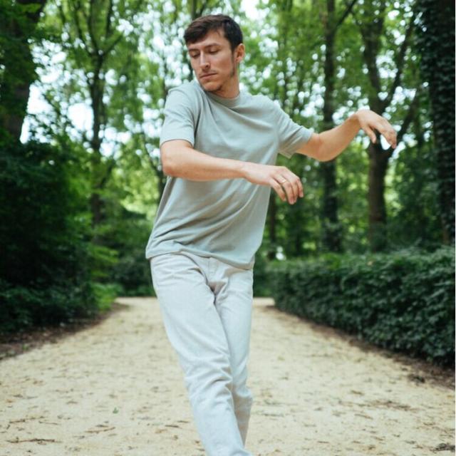 man twisting to the right and looking over right shoulder dancing outdoors in pale green shirt and light pants