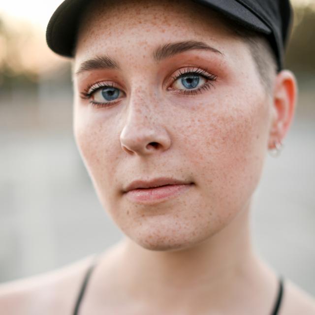 artist looking at camera with black top and black hat and shaved head
