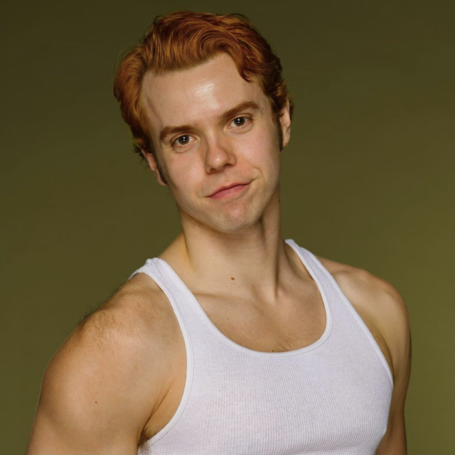 image of adrian wearing a white tanktop looking into the camera with an olive green background