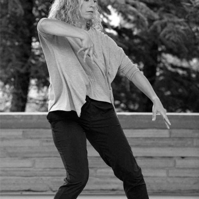 black and white photo of a dancer mid movement with short shoulder length hair and appears to be outside