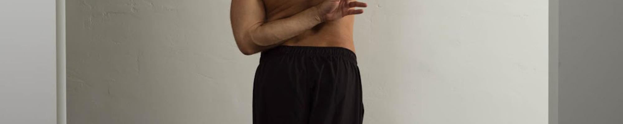 a photo of a dancer against a blank wall wearing black pants and shirtless in a tall extended pose. a small square overlay of kevin williamson covers the dancers head in a blue hue