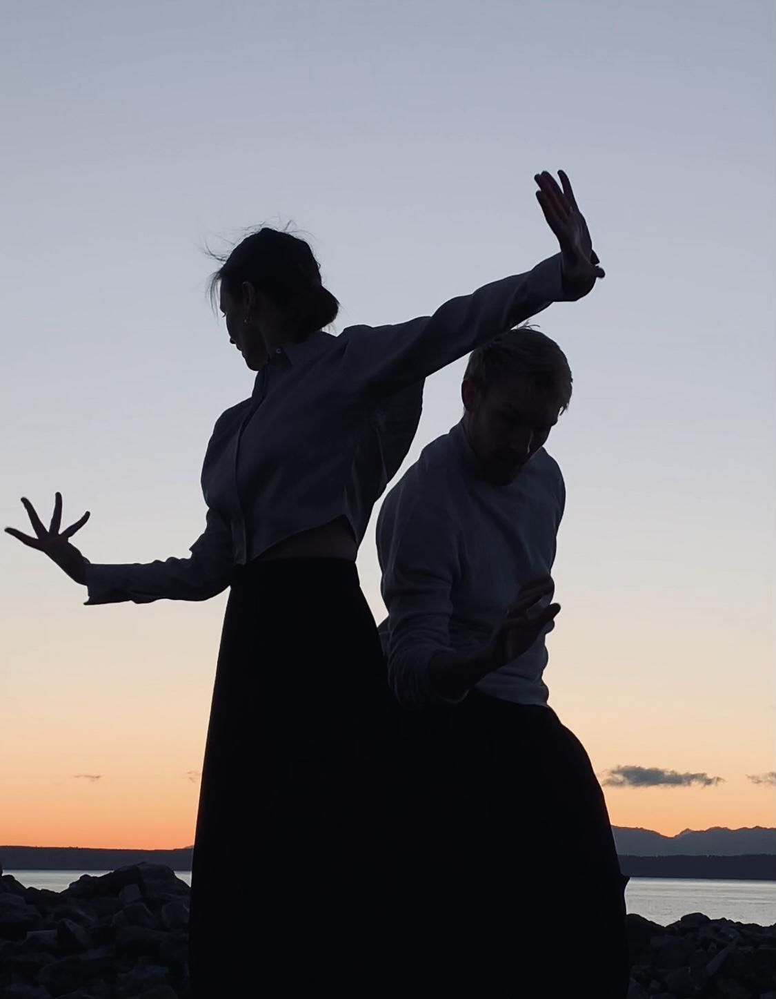 two dancers cast in silhouette against a pale grey and orange sky
