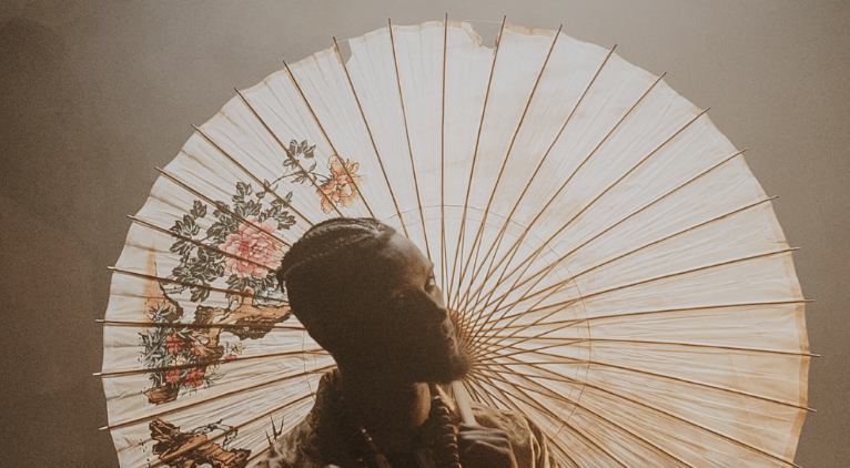 an image of a person with braids and a beard silhouetted in front of a large white umbrella with floral decoration