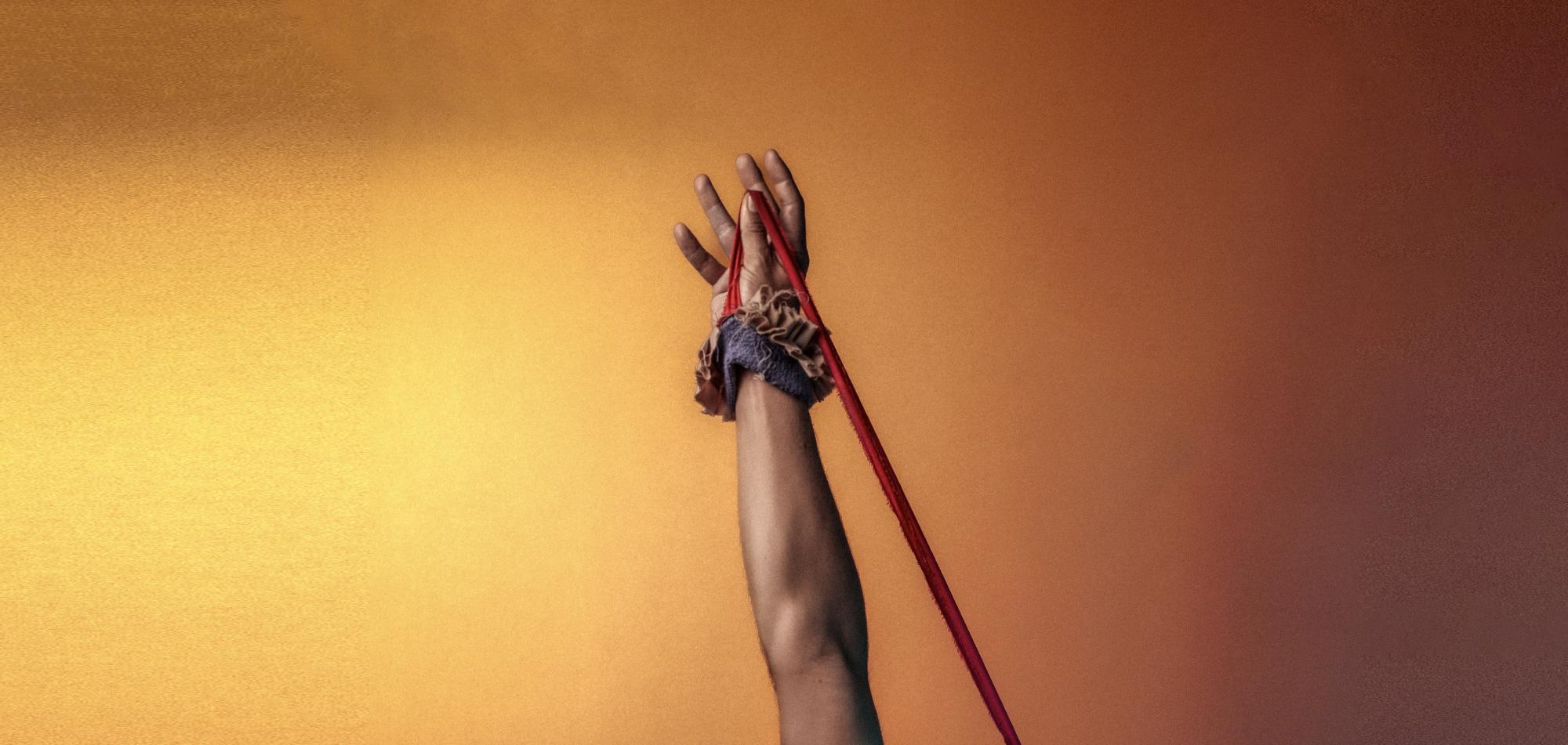 hand reaching up in a fist with string attached to a bracelet against an orange background