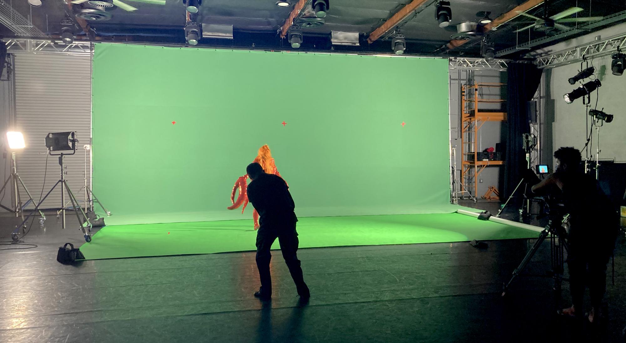 large warehouse with green backdrop and silouette of a person filming a subject in the background