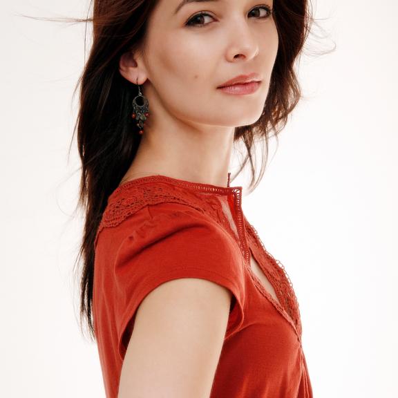 an image of a woman wearing a deep orange blouse against a white background. They are turned profile while their face is looking towards the camera