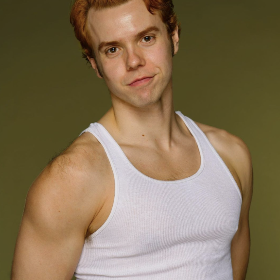 image of adrian wearing a white tanktop looking into the camera with an olive green background